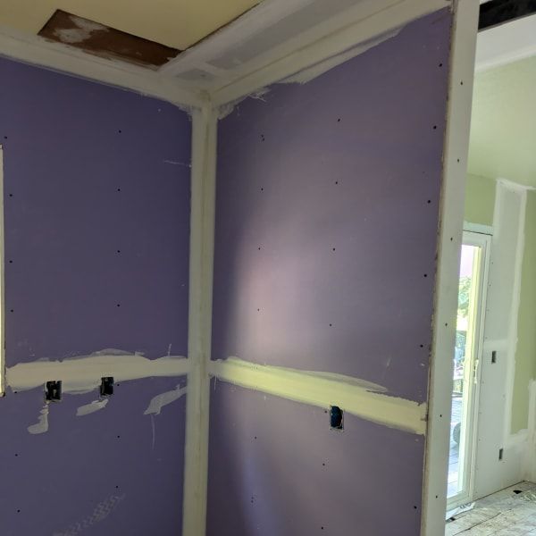 Purple drywall with taped seams in an unfinished interior room, with a doorway and hallway visible.