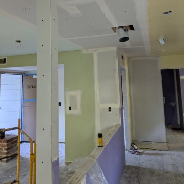 Interior under renovation with green and white walls, exposed drywall, and construction materials.
