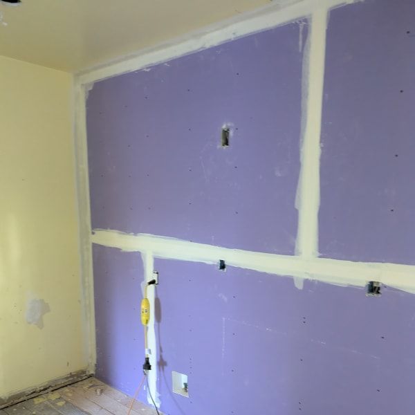 Purple drywall under renovation with white joint compound patches and exposed electrical openings