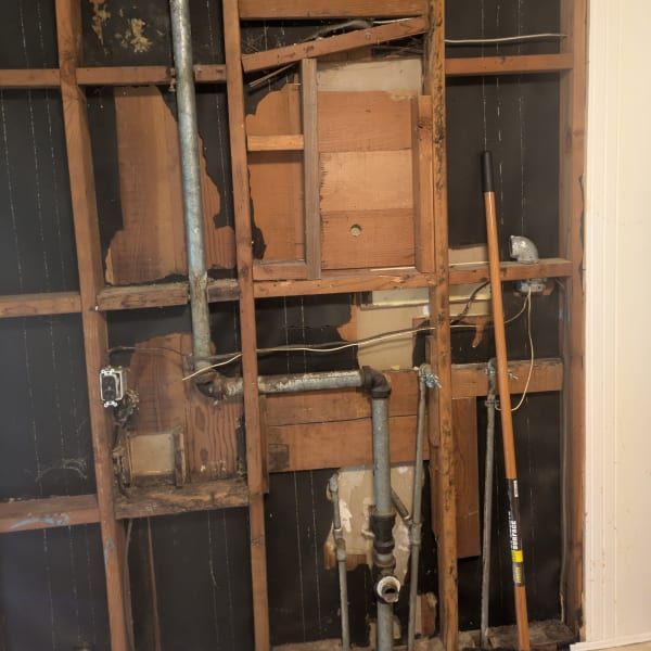 Exposed wall studs with plumbing pipes and tools in an unfinished interior wall demolition area