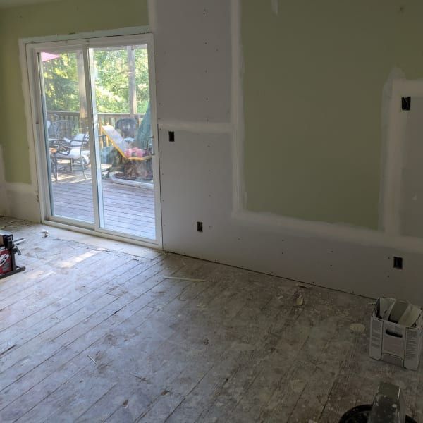 Unfinished room with drywall patches, bare wood floor, and sliding glass doors opening to a deck.