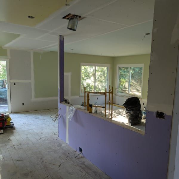Partially renovated room with drywall, purple accent wall, windows, and construction tools