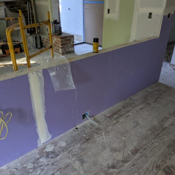 Partially renovated room with purple wall, patched drywall, open doorway, and construction materials on floor