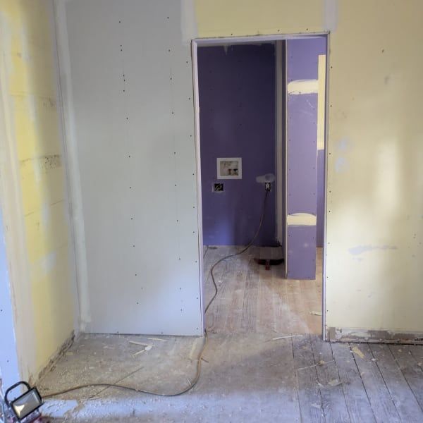 Partially renovated room with drywall, purple doorway, and exposed floor cords