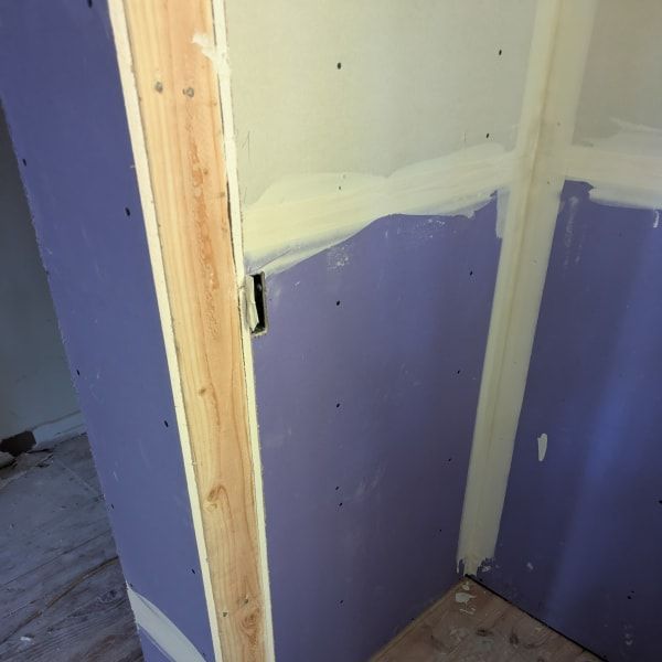 Partially finished room corner with purple drywall, white joint compound, and exposed wooden studs