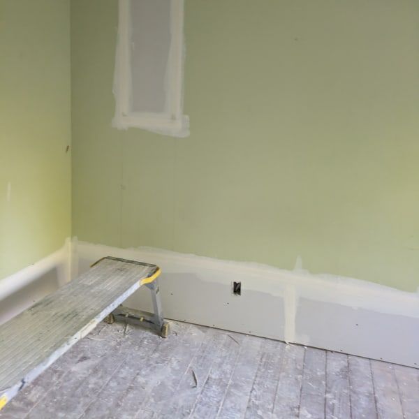 Partially renovated room with green walls, white trim, a step stool, and dust-covered floorboards