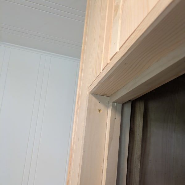 Close-up of a light wood door frame and white paneled wall