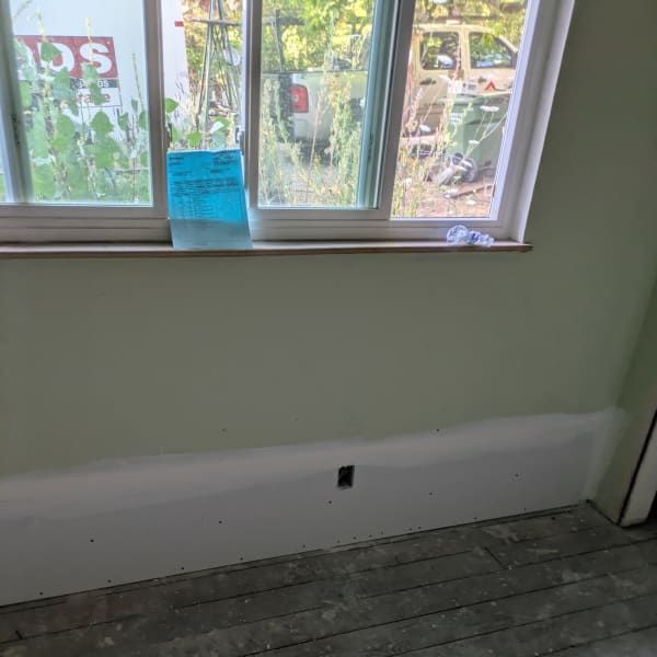 Empty room with pale green walls, worn wood floor, and a window with a blue note taped to it