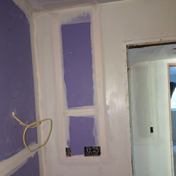 Partially painted interior wall with purple and white patches, outlet openings, and a doorway