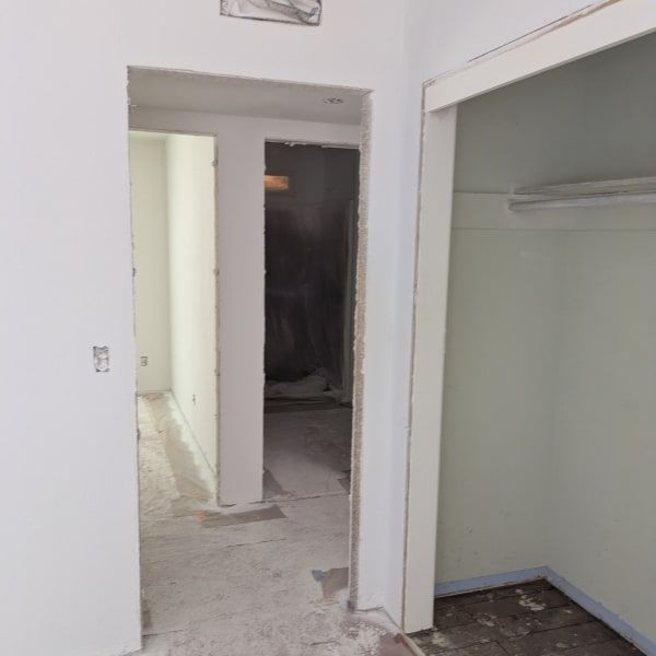 Partially renovated hallway with white walls, open doorways, and an empty closet area