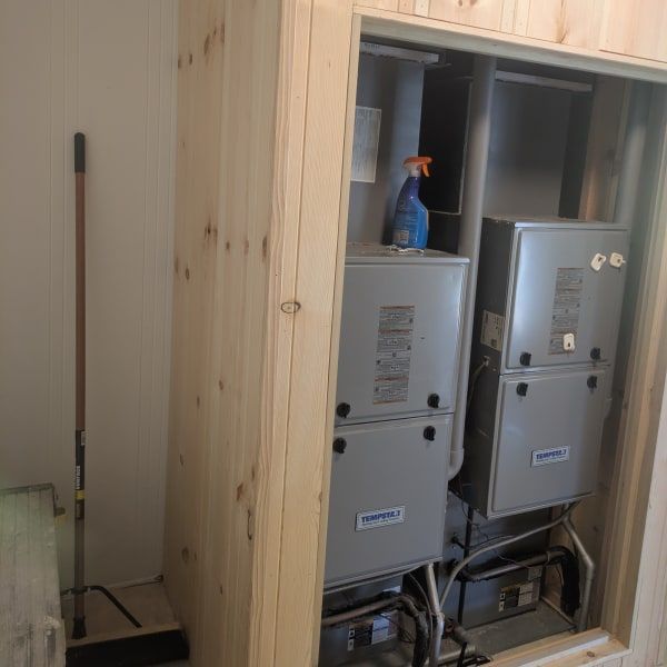 Indoor utility closet with two gray HVAC units and a blue spray bottle on a shelf.