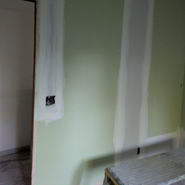 Partially painted green wall with white patching and an electrical outlet cutout near a doorway