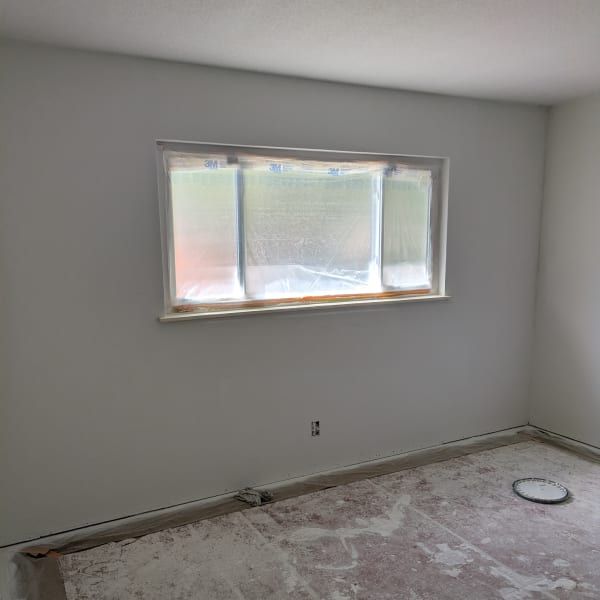 Empty room with gray walls, a small window, and unfinished floor with dust and paint marks