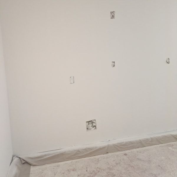 Bare white interior wall with a few electrical outlets and taped-off baseboard near a carpeted floor