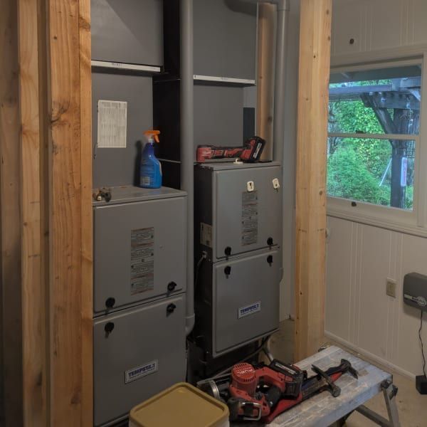 Utility closet with two gray furnace units, tools on top, and a window to the right.