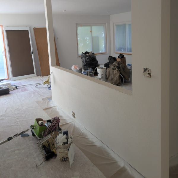 Interior room under renovation with plastic-covered floors, tools, and supplies near a half wall opening