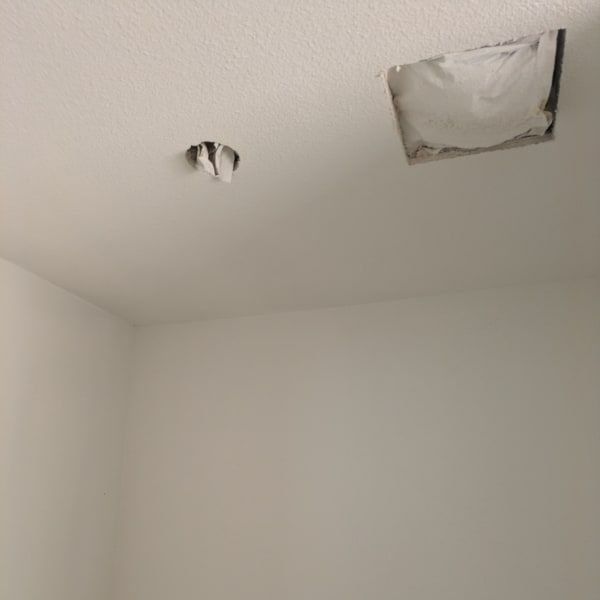 Ceiling with two damaged patches and a hanging light fixture in a white room