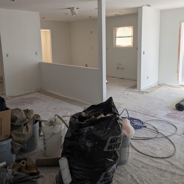 Renovation site with unfinished white walls, carpet, construction debris, and tools scattered on the floor.