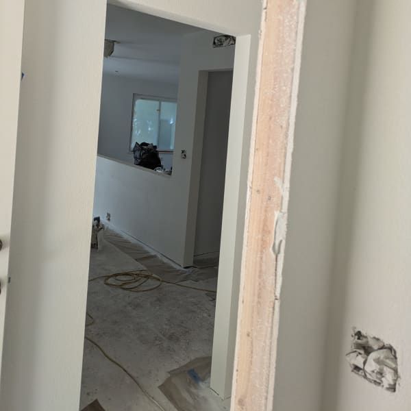 Narrow hallway under renovation with unfinished walls, floor cables, and a doorway into a room with a window.