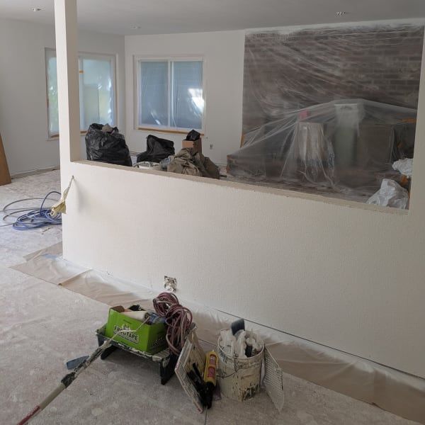 Living room under renovation with plastic-covered furniture, tools, and supplies on the floor
