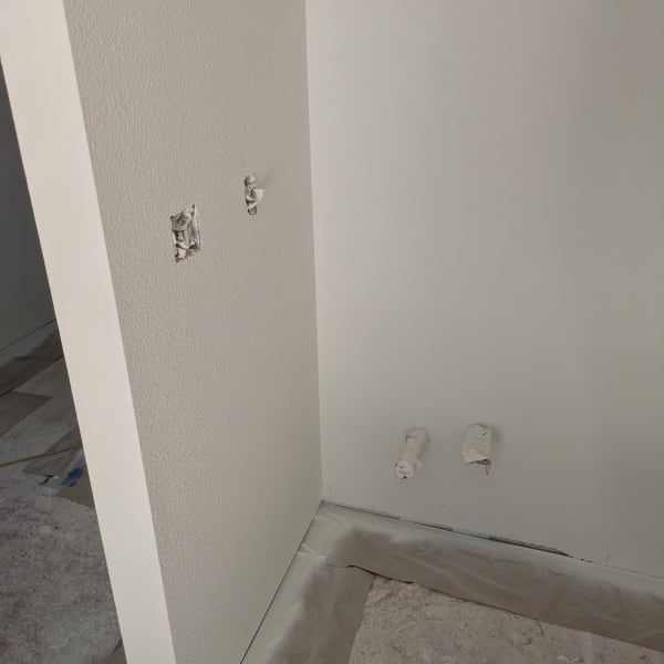Partially painted interior wall corner with patchy holes and unfinished baseboard area