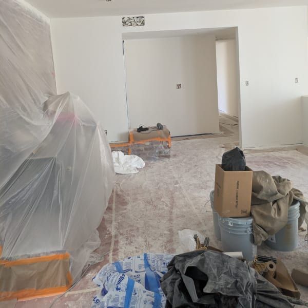 Dust-covered room under renovation with plastic-covered furniture and scattered tools on the floor