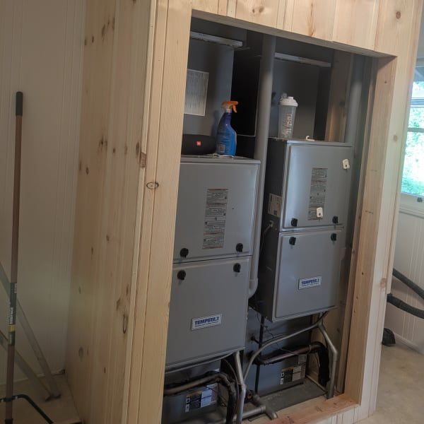 Open wall with two gray HVAC units inside a wooden cabinet frame