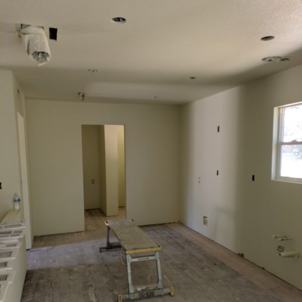 Empty beige room under renovation with unfinished floor, ladder, and window light