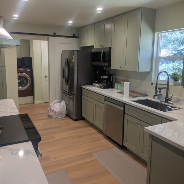 Modern kitchen with sage cabinets, stainless appliances, island, sink, and laundry visible in the background