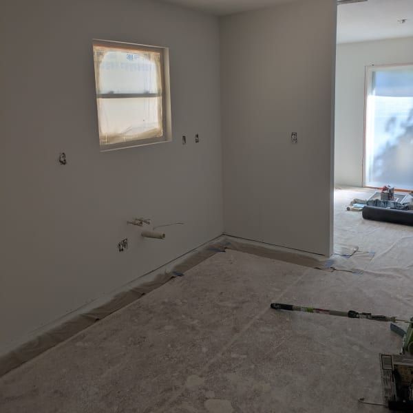 Empty room under renovation with bare walls, windows, and covered floor.