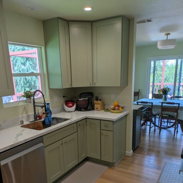 Kitchen with sage green cabinets, white countertops, and a view into a bright dining area
