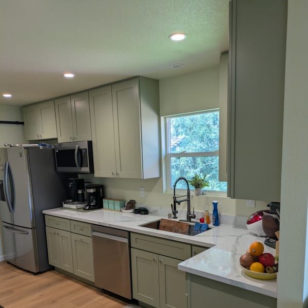 Modern kitchen with stainless appliances, pale cabinets, window over sink, and fruit on the counter