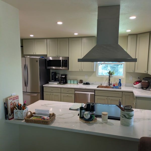 Modern kitchen with white countertops, beige cabinets, stainless fridge, and a large dark range hood.