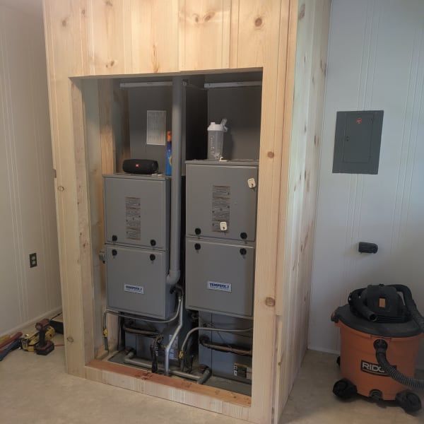 Two gray HVAC units inside a wood-framed closet, with a shop vacuum beside the opening.