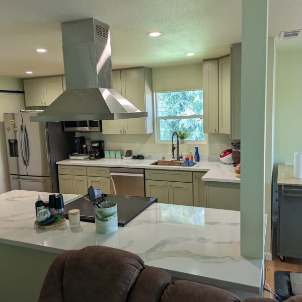 Modern kitchen with white cabinets, stainless range hood, marble island, and a window over the sink.
