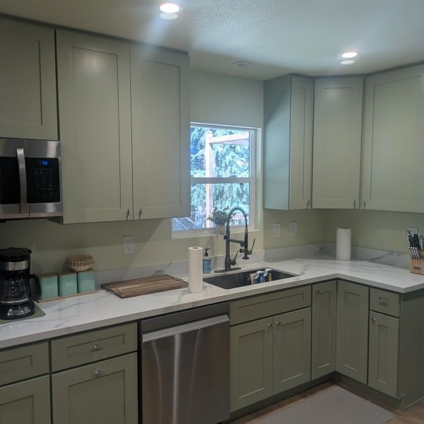 Modern kitchen with sage cabinets, white counters, stainless appliances, and a window over the sink