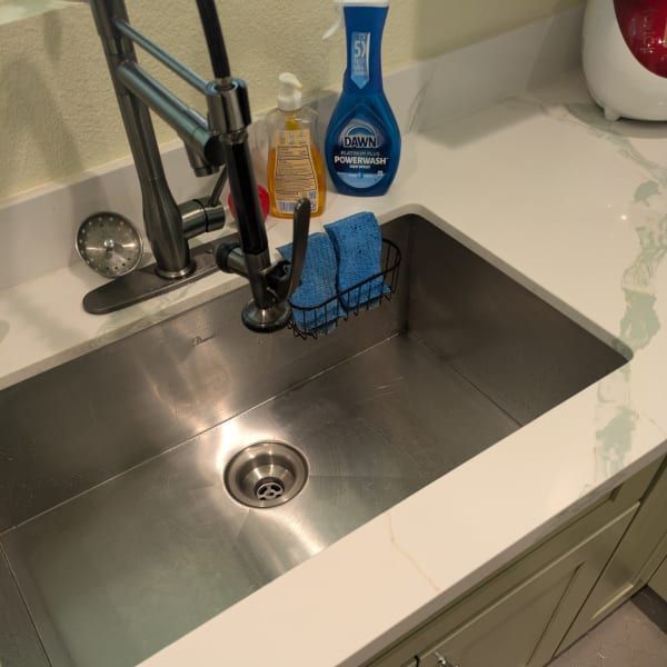 Stainless steel kitchen sink with faucet, blue soap bottle, sponge, and cleaning brush on the counter