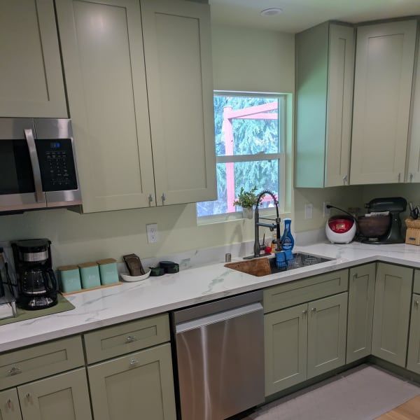 Modern kitchen with sage cabinets, stainless appliances, white countertops, and a window over the sink