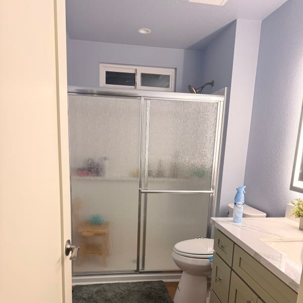 Small bathroom with a frosted-glass shower, toilet, and sink vanity in soft gray and beige tones