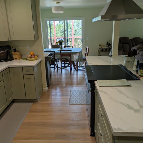 Modern kitchen with island, wood floors, and dining table by a window overlooking trees