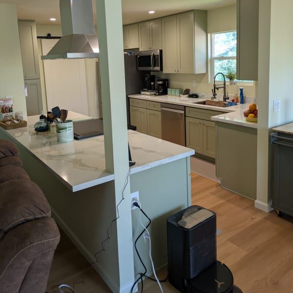 Modern kitchen with white island, beige cabinets, wood floor, and a brown sofa at left