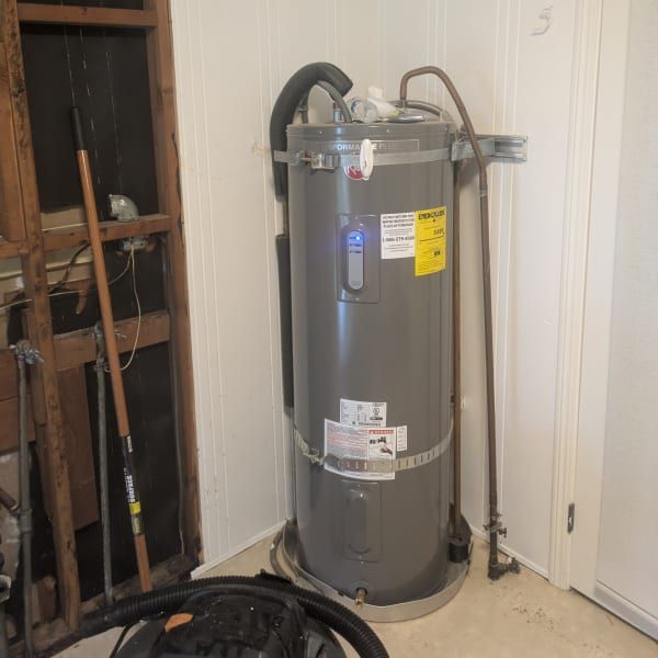 Gray water heater in a utility closet with pipes, hoses, and a white door.