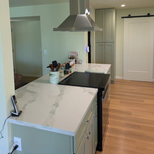 Modern kitchen with white countertops, stainless range hood, black stove, and light wood floors