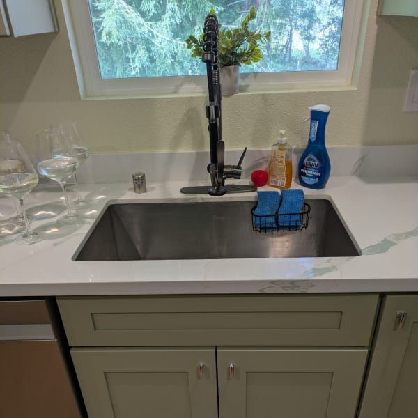 Kitchen sink under a window with soap, sponge, and glasses on the counter