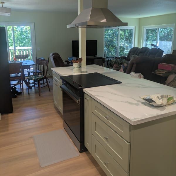 Modern kitchen with island, black stove, marble countertop, and open living room with sofa and dining table.