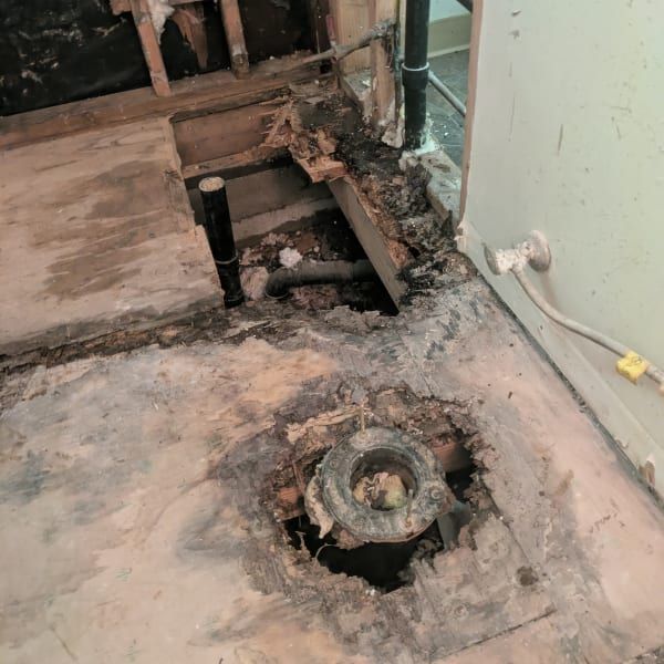 Damaged floor with exposed drain pipe and water-stained wall in a bathroom under renovation