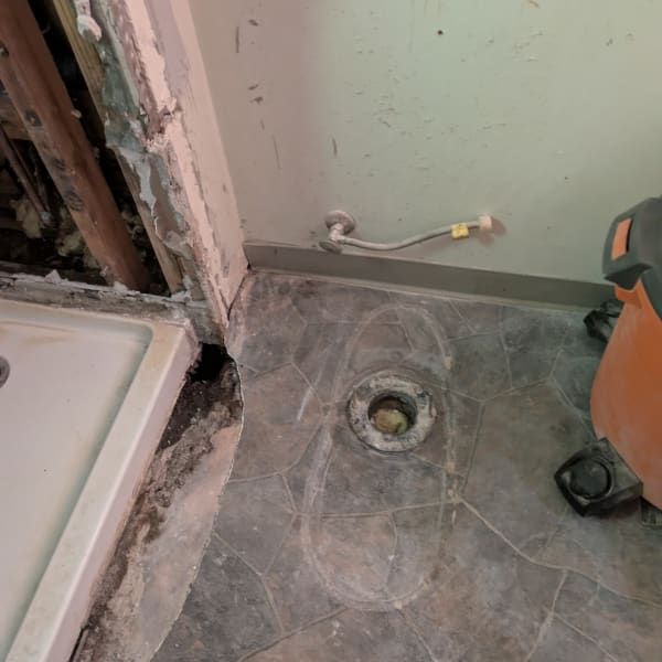 Bathroom floor with a drain opening, exposed wall plumbing, and construction debris near a shower area