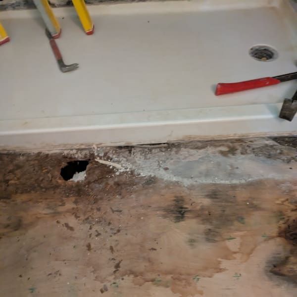 Damaged floor under a sink with a hole, peeling stains, and tools on the counter above