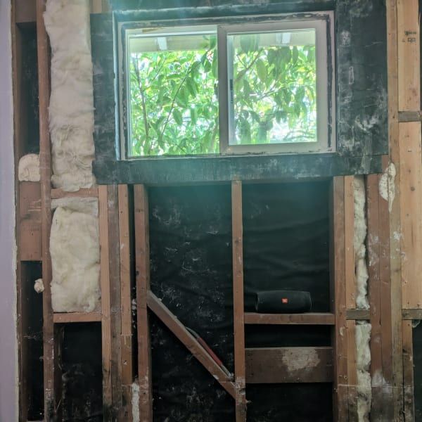 Partially gutted wall with a small window and exposed wood framing in a renovation area
