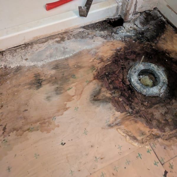 Damaged bathroom floor with burnt, water-damaged wood around a drain opening